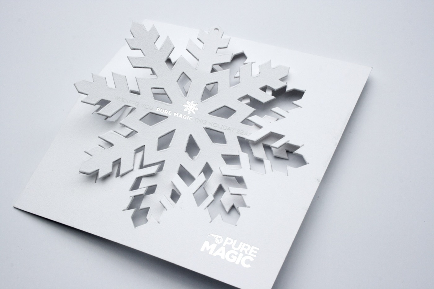 A white laser die-cut snowflake card standing away from its backing sheet