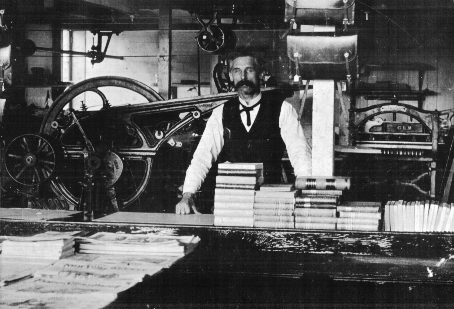 J.B. Lawton, our founder, at a hand-fed press beside stacks of finished books, 1900