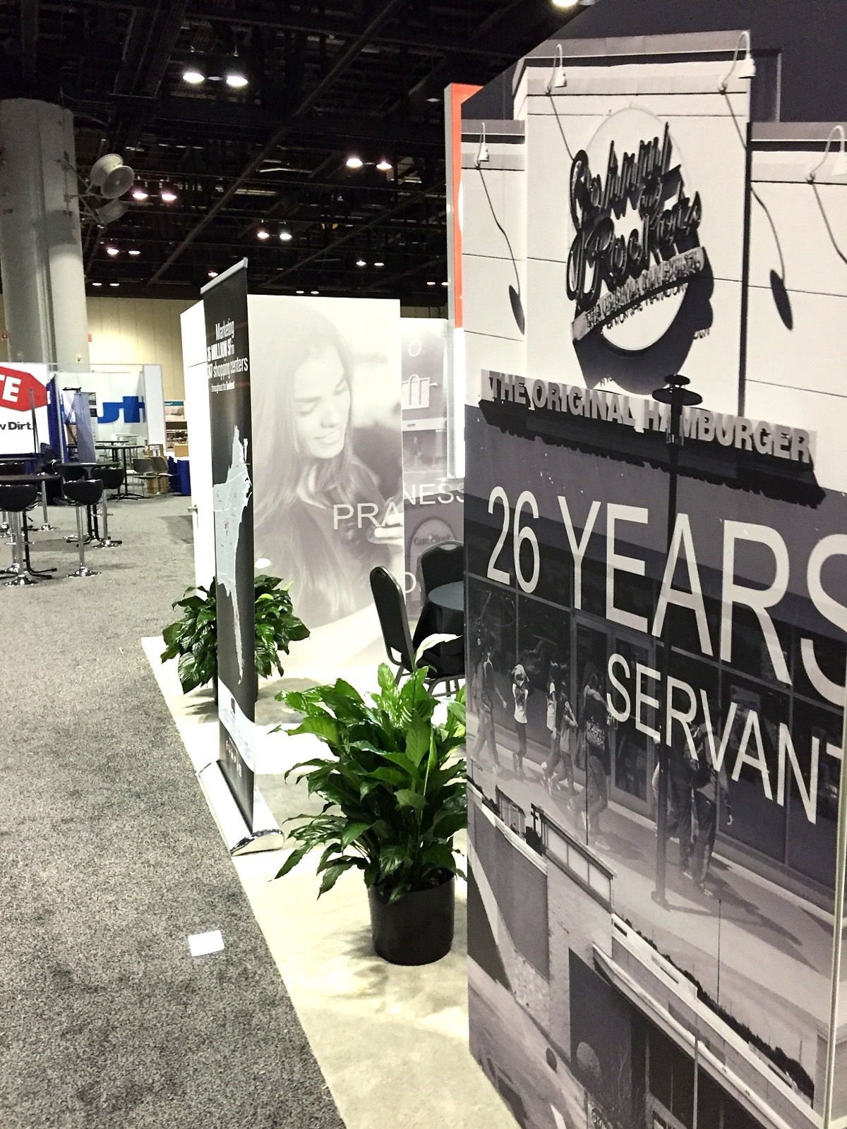 A trade show booth corner with tall black and white panels reading 26 Years Servant
