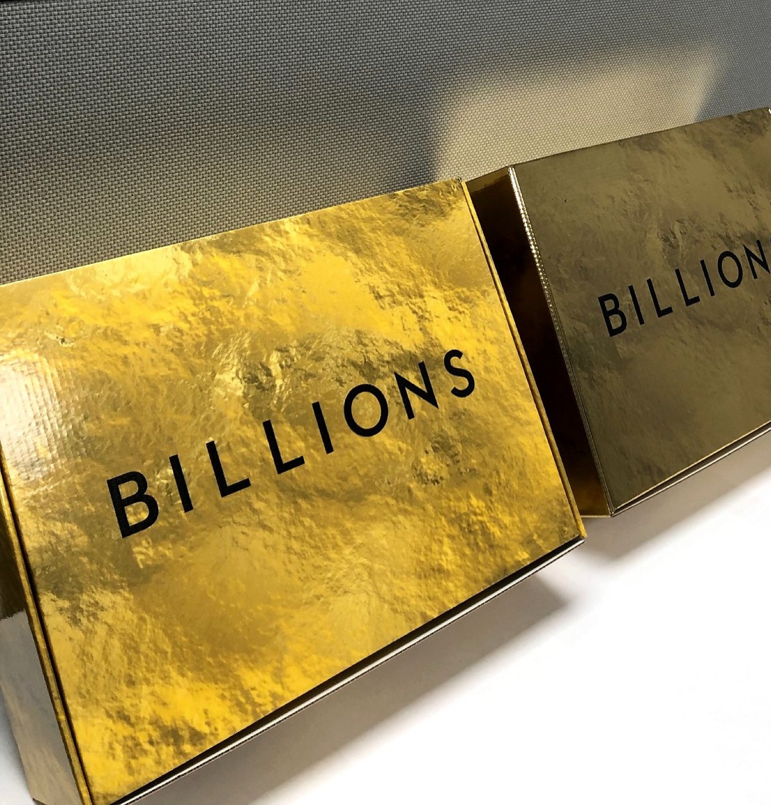 Two hammered gold foil boxes printed with the word Billions